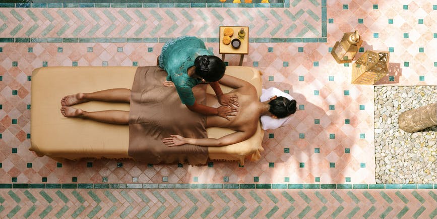Fotografía aérea de una mujer anónima recibiendo un masaje balinés en un hermoso spa de día. Combinación de colores pastel.