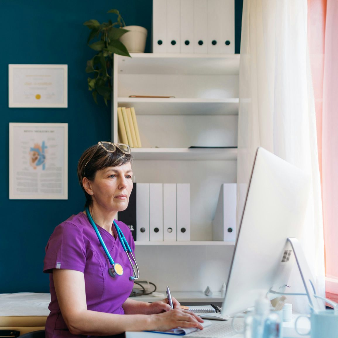 Una profesional médica con un uniforme morado trabajando en su escritorio frente a una computadora en su oficina
