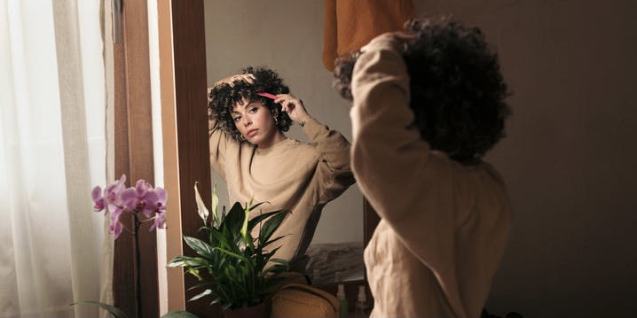 Grooming routine of a young Black woman with curly brown hair. She is styling her hair by picking her curls with a long comb.