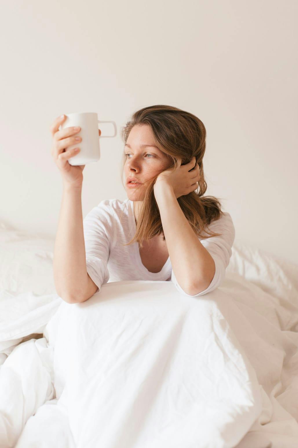 Woman sitting up in bed, holding a hot drink, sick with Covid