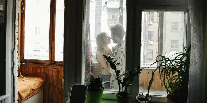A couple kisses on the porch of their apartment as seen through hazy windows.