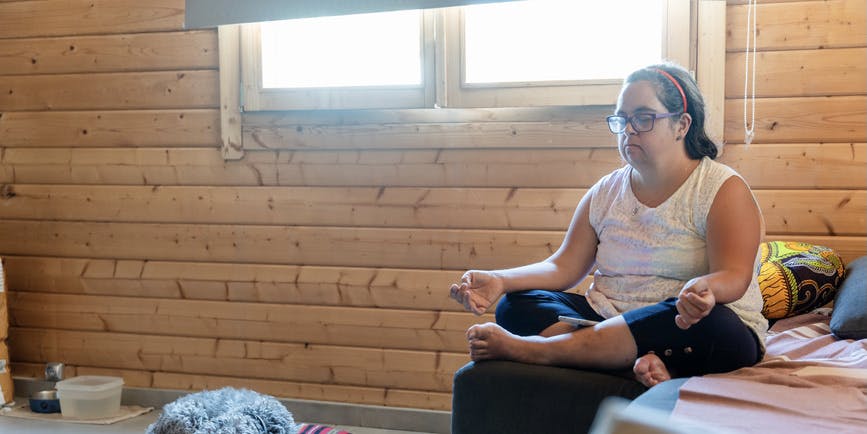 A woman with Down syndrome finds solace in meditation within the confines of her room.