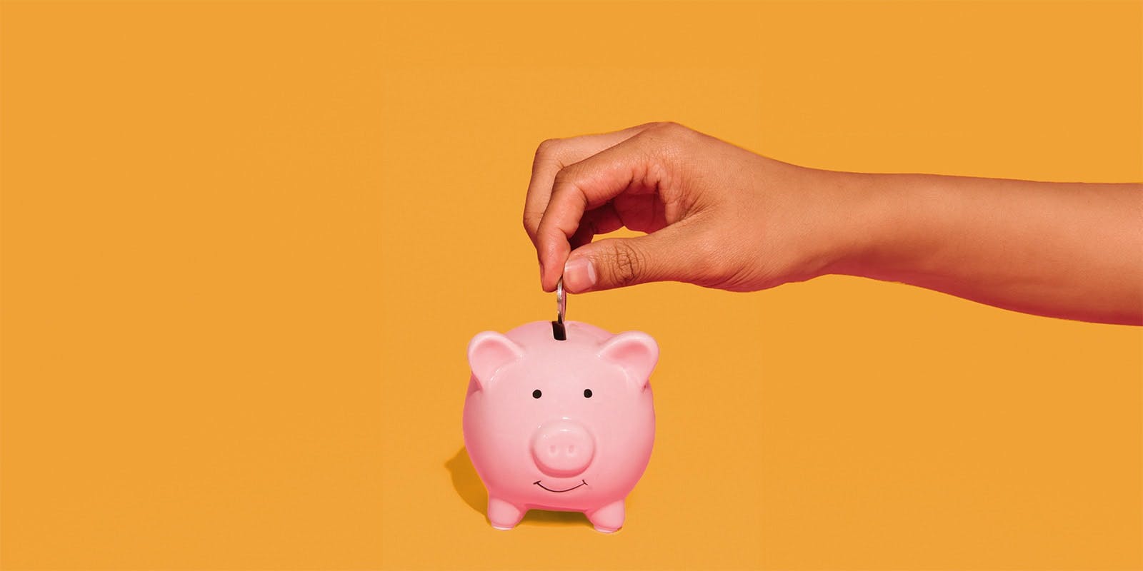 A hand putting a coin into a pink piggy bank