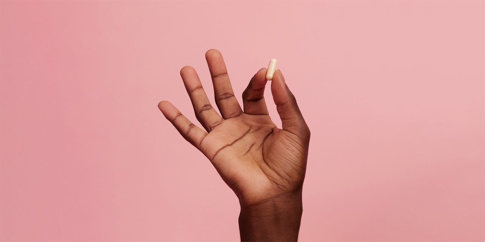 A dark female hand holding up a pill pinched between index finger and thumb