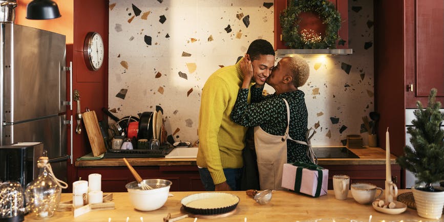 Mature Hispanic woman kissing a young male on the cheek during Christmas dinner preparation in a festive kitchen at home.