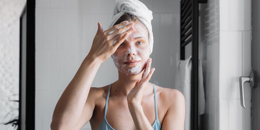 Mujer bonita de unos veinte años lavándose la cara con jabón en el baño.