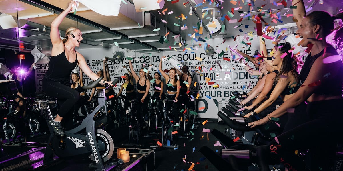 A celebratory photo of a SoulCycle class with a group of riders cheering and confetti flying through the air. Photo courtesy of SoulCycle.