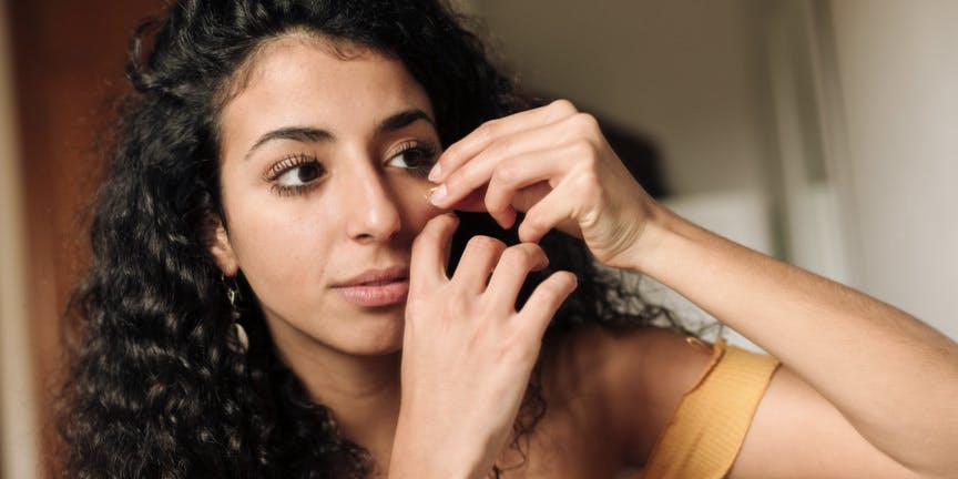 Young woman with olive skin, applying essential oil to hydrate her face as part of her beauty routine.