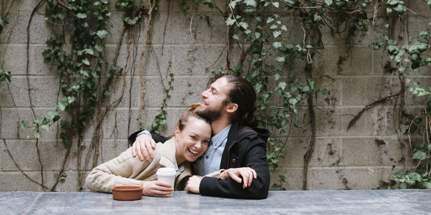 Young couple hugging and smiling while sitting in outdoor patio of coffee shop