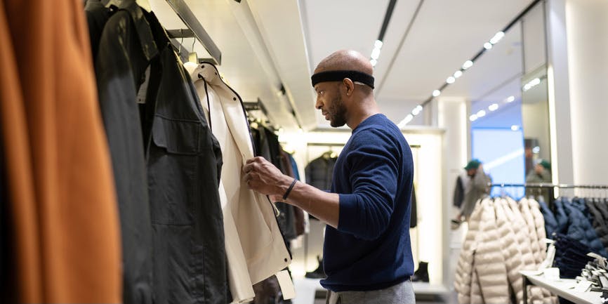 Black man wearing casual clothes after hair transplant procedure looking for clothes in the fashion store. He has bandanna on his head. Shopping concept.