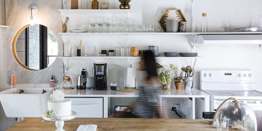 A modern country kitchen with open shelves, a wood countertop and a woman walking by in a blur.